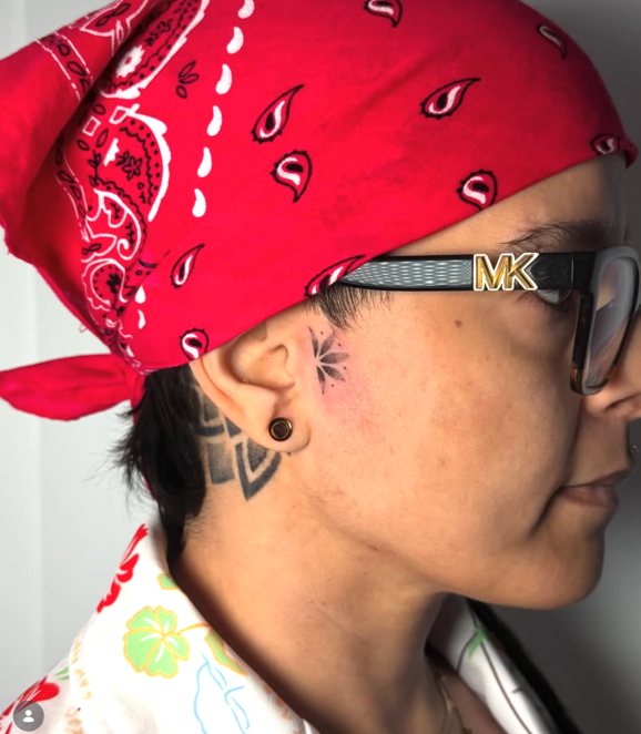 Tiny fine line flower tattoo beside the ear, hand poked