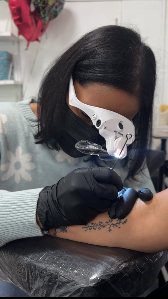 Sheila hand poking a fine line tattoo on a forearm